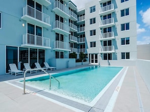 A modern building with a pool area, including a pool, lounge chairs, and a staircase leading to the upper floors. - Landing | Stylish 1BD, Gym (Hialeah)