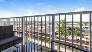 A balcony with a view of a train yard and palm trees. - Landing | Stylish 1BD, Gym (Hialeah)