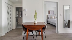 Quarto de hotel moderno com uma mesa de jantar de madeira, um vaso com planta, uma cama com roupa de cama branca e um espelho grande.