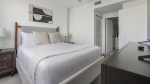 Ein ordentlich eingerichtetes Schlafzimmer mit einem Bett, Nachttischen, einer Lampe, einem Spiegel und einer Tür zu einem Badezimmer.