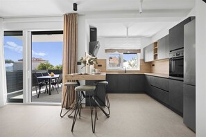 A modern kitchen with a dining area, a large window, and a view of the outside. - Villa Lucis Kaštela | Private Pool and sea view Villa near Split (Kaštel Kambelovac)