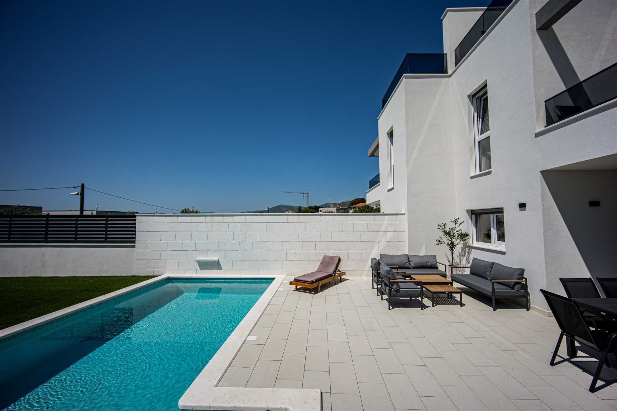 A modern outdoor pool area with a rectangular pool, lounge chairs, and a patio table.