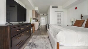 Ein modernes Hotelzimmer mit einem großen Bett, einem Fernseher auf einer Kommode, einem Schreibtisch und einer Küchenzeile.