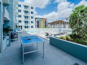 Un espace piscine aménagé sur le toit, avec des chaises longues, une table de ping-pong et une vue sur les bâtiments environnants.