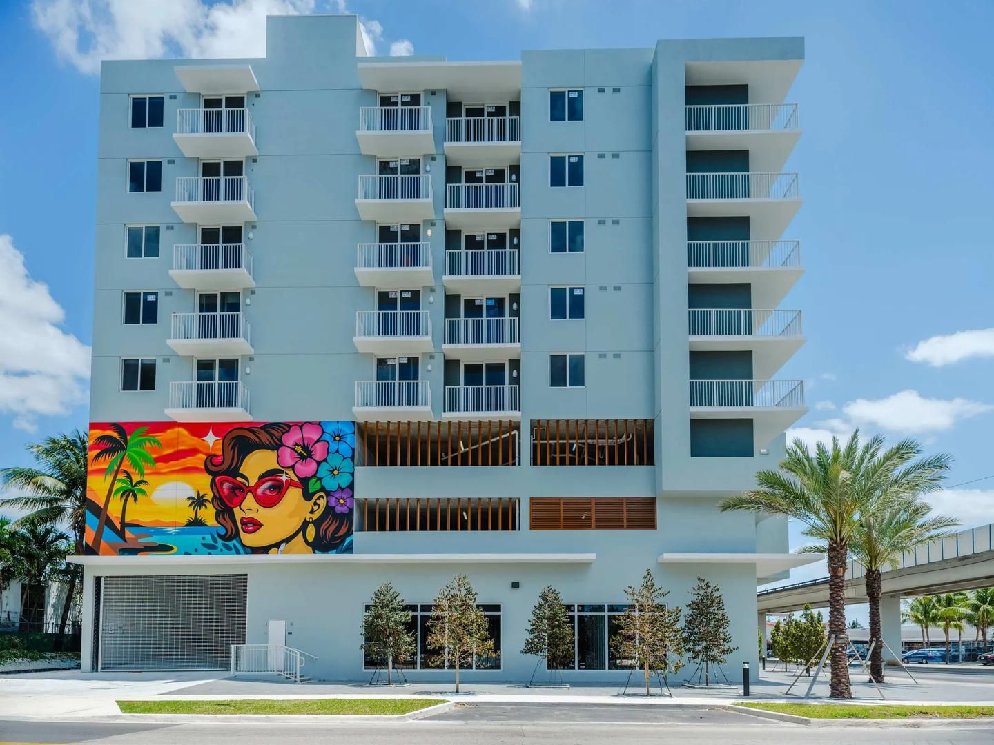 A multi-story hotel with balconies, a mural, and palm trees.