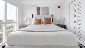 A hotel room with a large bed, two bedside tables with lamps, a window with a view, and a red object on the wall.