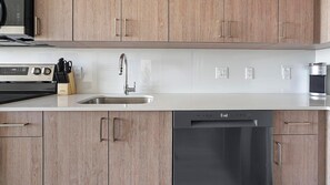 A modern kitchen with wooden cabinets, a stainless steel sink, a dishwasher, and a coffee machine.