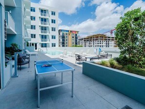 A rooftop pool area with lounge chairs, a ping pong table, and a view of surrounding buildings. - Landing | Modern 2BD, Gym (Hialeah)