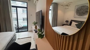 Habitación de hotel con cama, escritorio, televisor, espejo y balcón con vista a edificios.