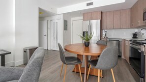 A modern kitchen with wooden cabinets, a stainless steel refrigerator, and a dining area with a round wooden table and chairs. - Landing | Chic 2BD, Gym (Hialeah)