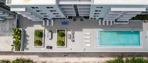 An aerial view of a hotel with a swimming pool, outdoor seating, and a parking area. - Landing | Stunning 1BD, Gym (Hialeah)
