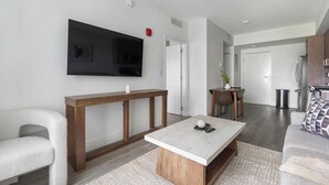 Een moderne woonkamer met een flatscreen televisie, een houten salontafel, een bank en een eethoek met een tafel en stoelen.