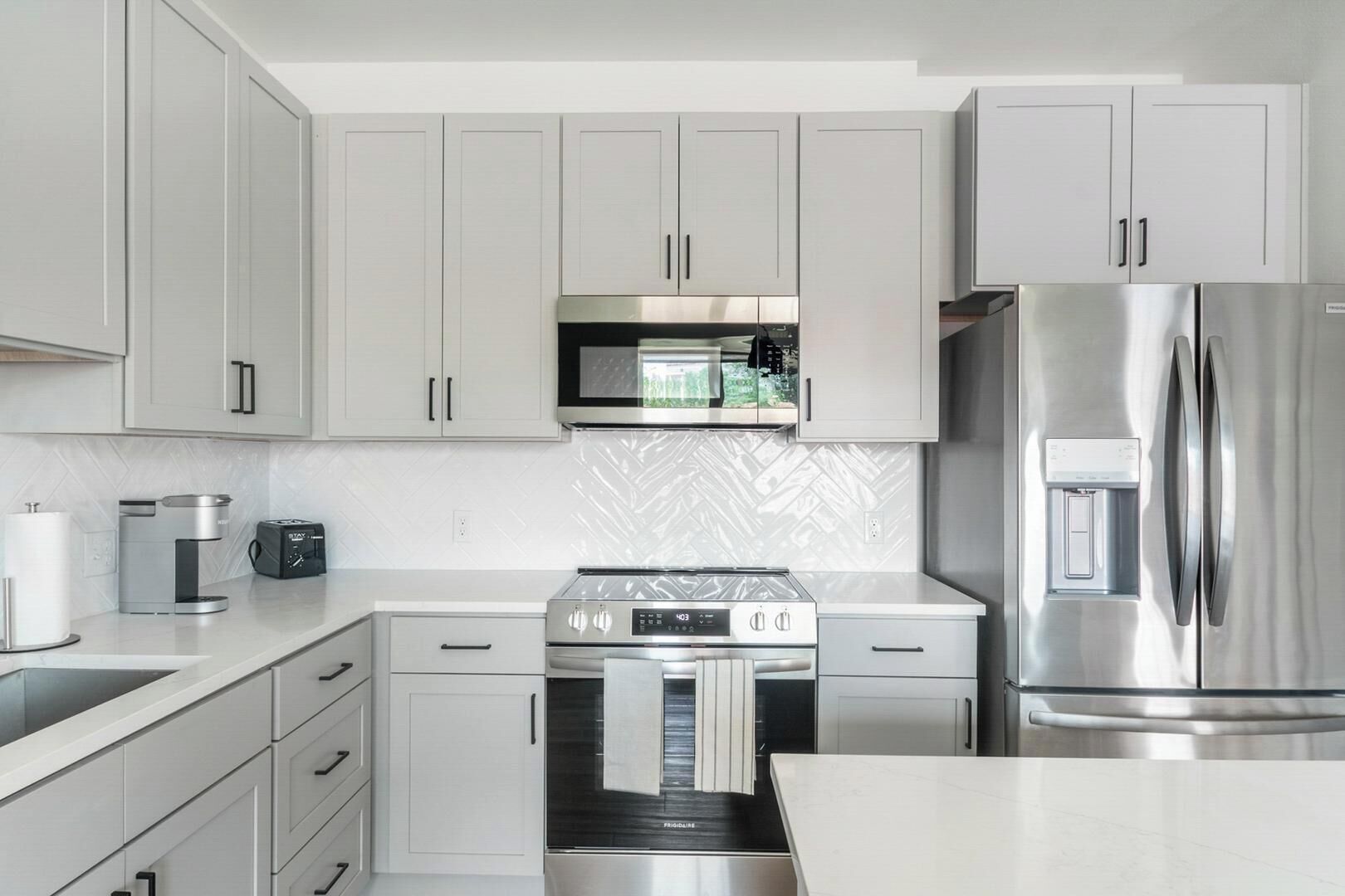 A modern kitchen with white cabinets, a stainless steel refrigerator, a built-in oven, and a microwave.