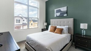 Ein Schlafzimmer mit großem Fenster, einem Bett mit weißer Bettwäsche, zwei Nachttischen mit Lampen und einer grünen Akzentwand.