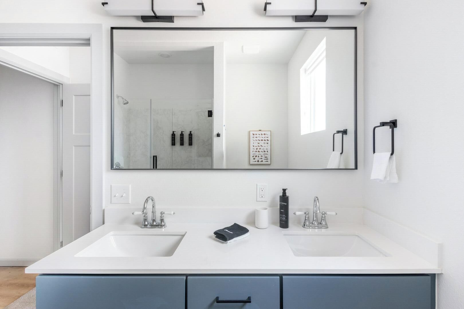 Une salle de bain moderne avec deux lavabos, un grand miroir et un porte-serviettes.