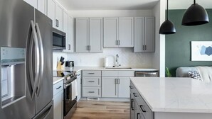Eine moderne Küche mit Edelstahlgeräten, grauen Schränken, einer Fischgrät-Fliesenrückwand und Pendelleuchten.
