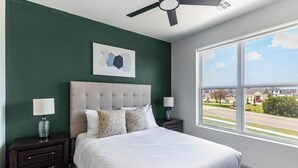 Ein Schlafzimmer mit einem Bett, zwei Nachttischen, einem Deckenventilator, einem Fenster mit Aussicht und einem an der Wand hängenden abstrakten Kunstwerk.