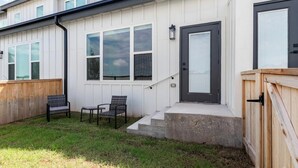 Une maison moderne avec un porche à l’avant, une porte et deux chaises.