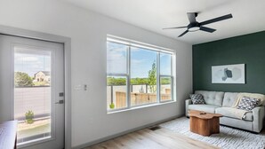Un salon moderne doté d’une porte-fenêtre coulissante, d’un ventilateur de plafond, d’un canapé gris et d’une table basse en bois.