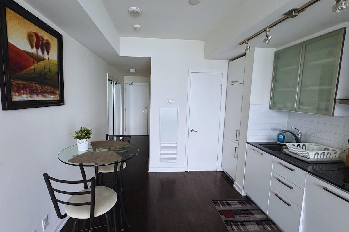 A compact kitchen with white cabinets, a black countertop, and a small dining area with a glass table and chairs.