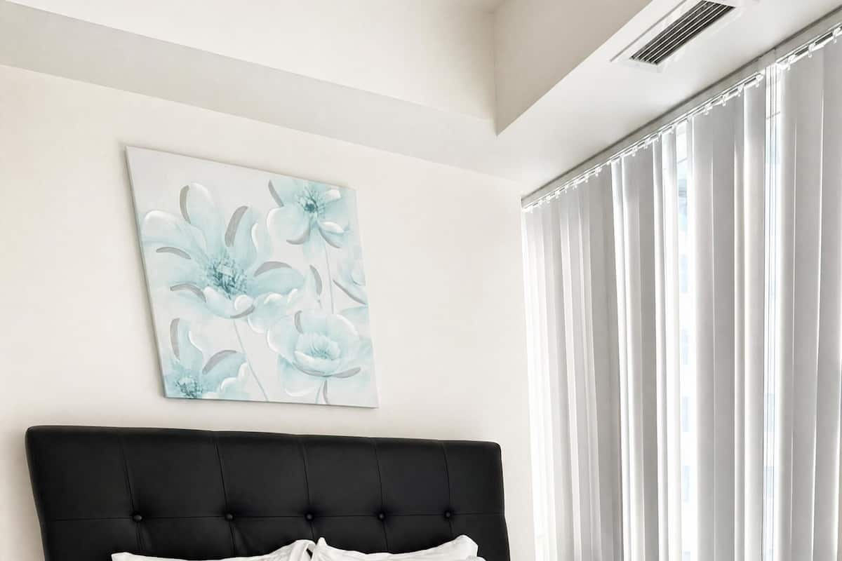 A neatly made bed with white linens and pillows, a black upholstered headboard, and a floral artwork on the wall.