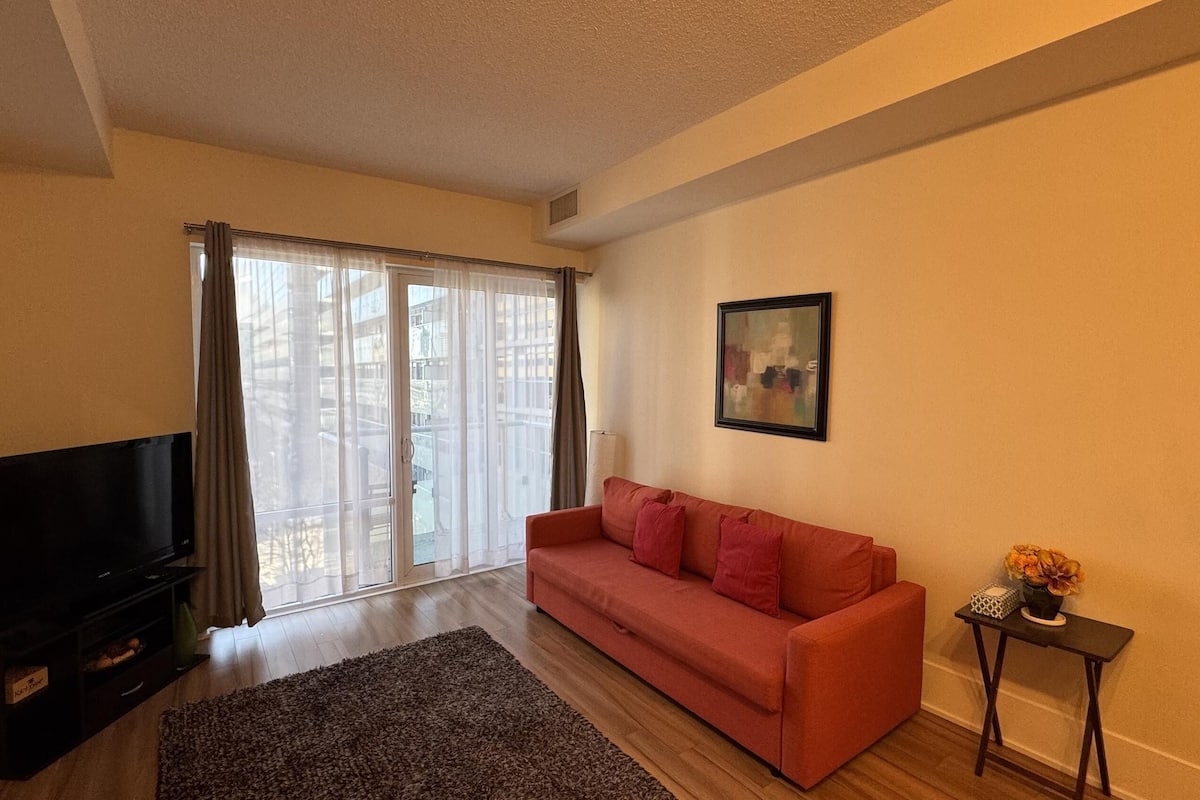 A living room with a sofa, a TV, a window with curtains, and a framed picture on the wall.