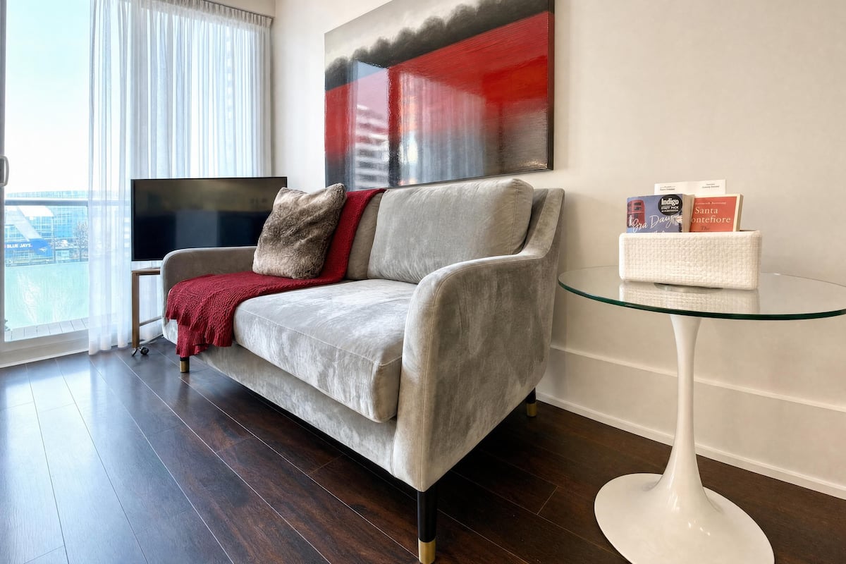 A modern living room with a grey sofa, a red throw blanket, a glass coffee table, and a flat-screen TV.