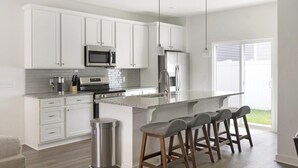 A modern kitchen with white cabinets, stainless steel appliances, a granite countertop, and a bar stool area.