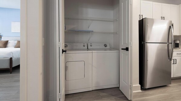 A compact kitchen with a stainless steel refrigerator, a built-in oven, and a washing machine. - Landing | Spectacular Studio, Pool, Clubhouse (Dallas)