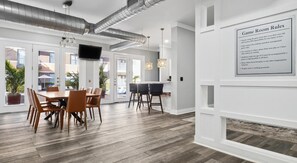 Ein moderner Spielraum mit einem Holztisch, Stühlen, einem Fernseher und einem an der Wand befestigten Regelzeichen.