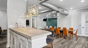 A modern kitchen with a central island, dining area with chairs, and a TV mounted on the wall. - Landing | Spectacular Studio, Pool, Clubhouse (Dallas)