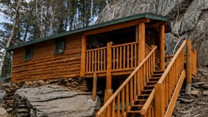 A log cabin with a wooden staircase leading to a porch. - Cozy 2BR Little Cabin | 15 Minutes to Mt. Rushmore (Rapid City)