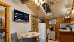 A cozy, wooden interior with a dining area, kitchen, and a TV displaying a Netflix show. - Cozy 2BR Little Cabin | 15 Minutes to Mt. Rushmore (Rapid City)