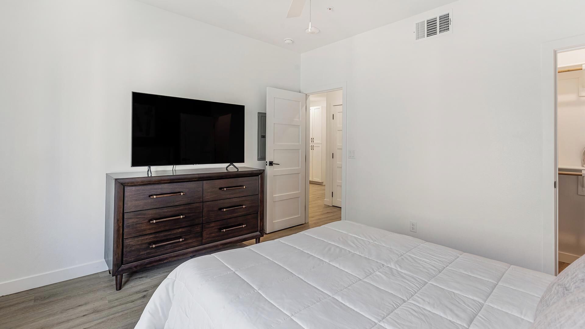 Une chambre à coucher comprenant un lit, une commode, un téléviseur et une porte donnant sur une autre pièce.