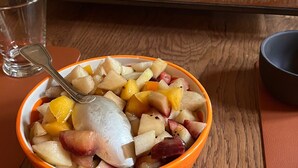 Morgenmad med en skål frugtsalat, et croissanter og et glas juice på et træbord.