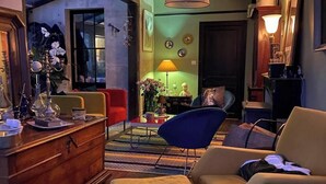 En hyggelig stue med et træskab, en blå stol, en beige lænestol og en rød stol. Der er en lampe på et sofabord og en vase med blomster.