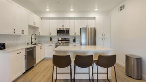 Een moderne keuken met witte kastjes, roestvrijstalen apparatuur en een centraal eiland met barkrukken.
