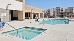 Un espace piscine comprenant deux piscines, un bâtiment à la façade beige et un ciel d’un bleu éclatant.