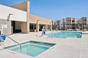 A pool area with two pools, a building with a beige facade, and a clear blue sky. - Landing | Amazing 2BD, Pool, Gym (North Las Vegas)