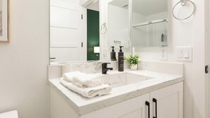 A bathroom with a white marble sink, black faucet, and a mirror above it. There are two bottles of hand soap on the sink and a potted plant on the counter. - Landing | Beautiful 2BD, Clubhouse, Pool (North Las Vegas)