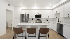 Una cocina moderna con armarios blancos, electrodomésticos de acero inoxidable y una isla central con taburetes de bar.