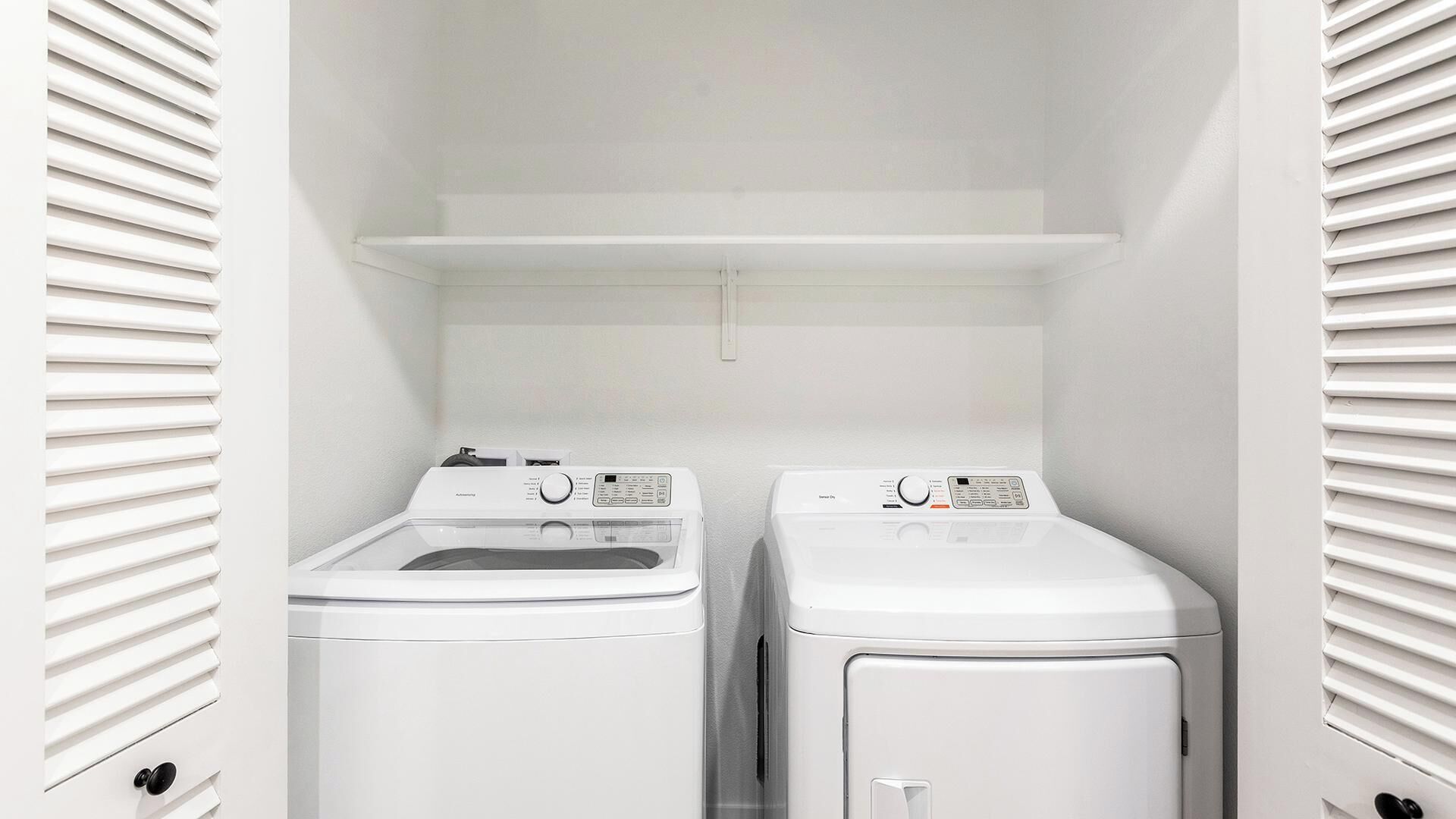 Une petite buanderie avec deux machines à laver blanches et une étagère au-dessus.