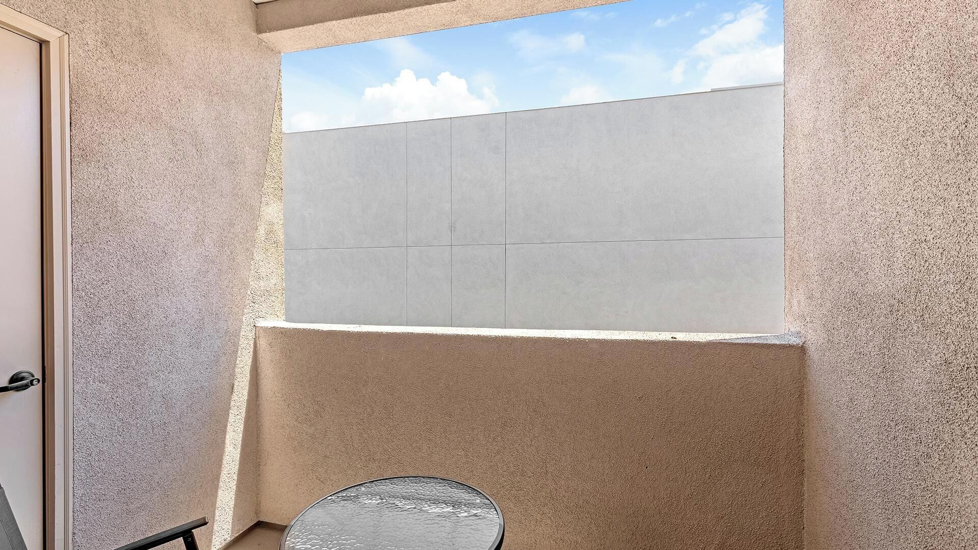 A small, enclosed balcony with a view of the sky and a door to the left.