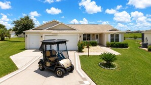 Une maison d’habitation avec un garage, une allée et un véhicule de golf garé devant.