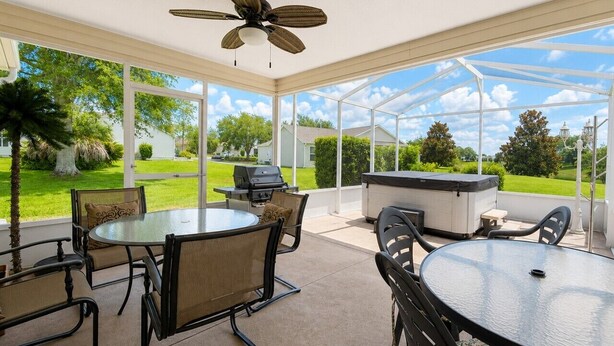 Un patio couvert avec une table ronde et des chaises, un ventilateur de plafond et un barbecue.