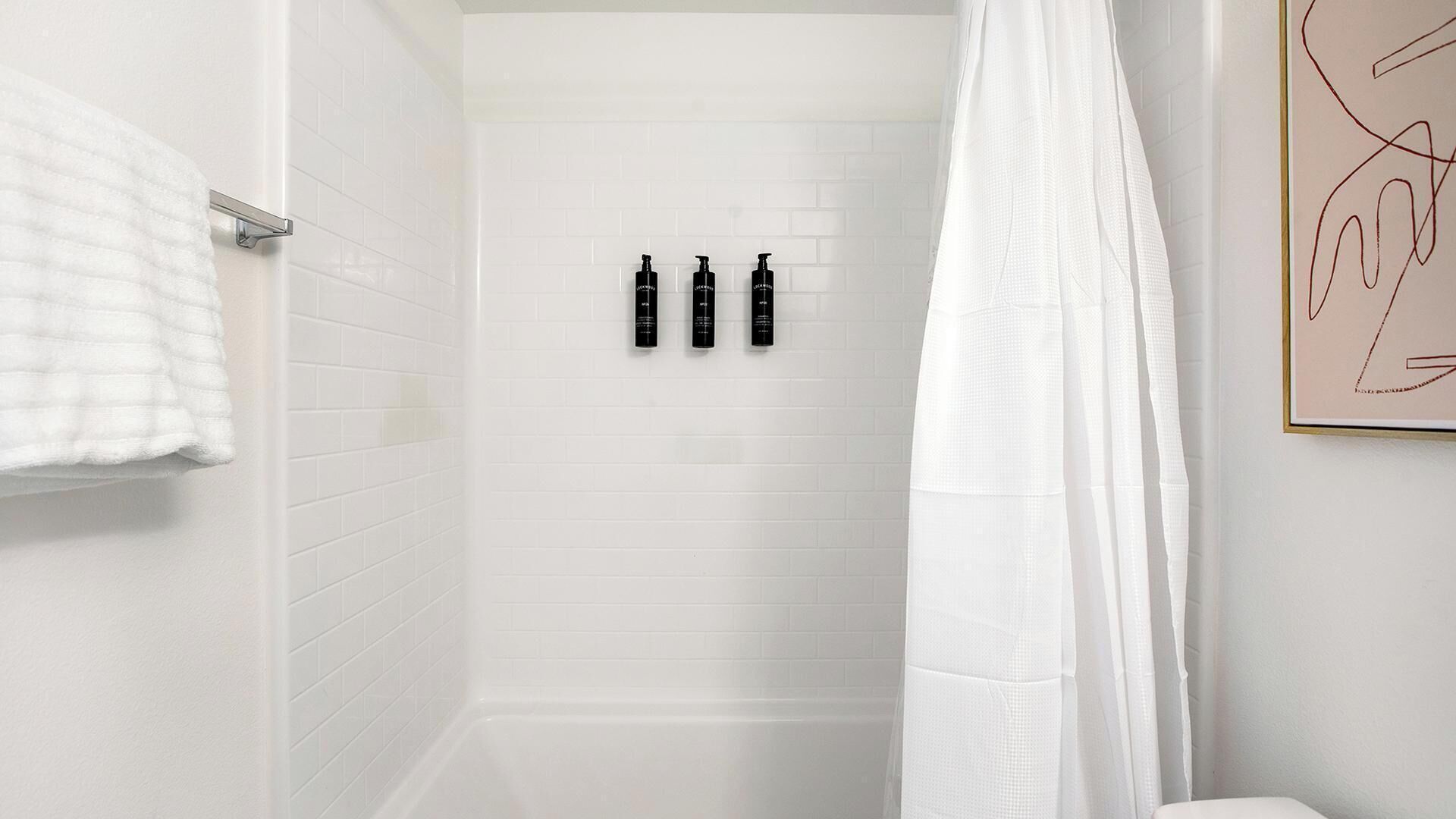 Un bagno con pareti piastrellate in bianco, una tenda da doccia e tre bottiglie nere appese al muro.