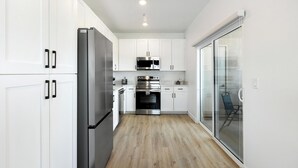 A modern kitchen with white cabinets, stainless steel appliances, and a wooden floor. - Landing | Amazing Studio, Clubhouse, Gym (North Las Vegas)