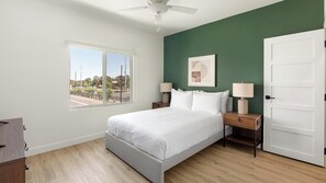 Um quarto com cama, mesas de cabeceira, ventoinha no teto, janela com vista e porta.