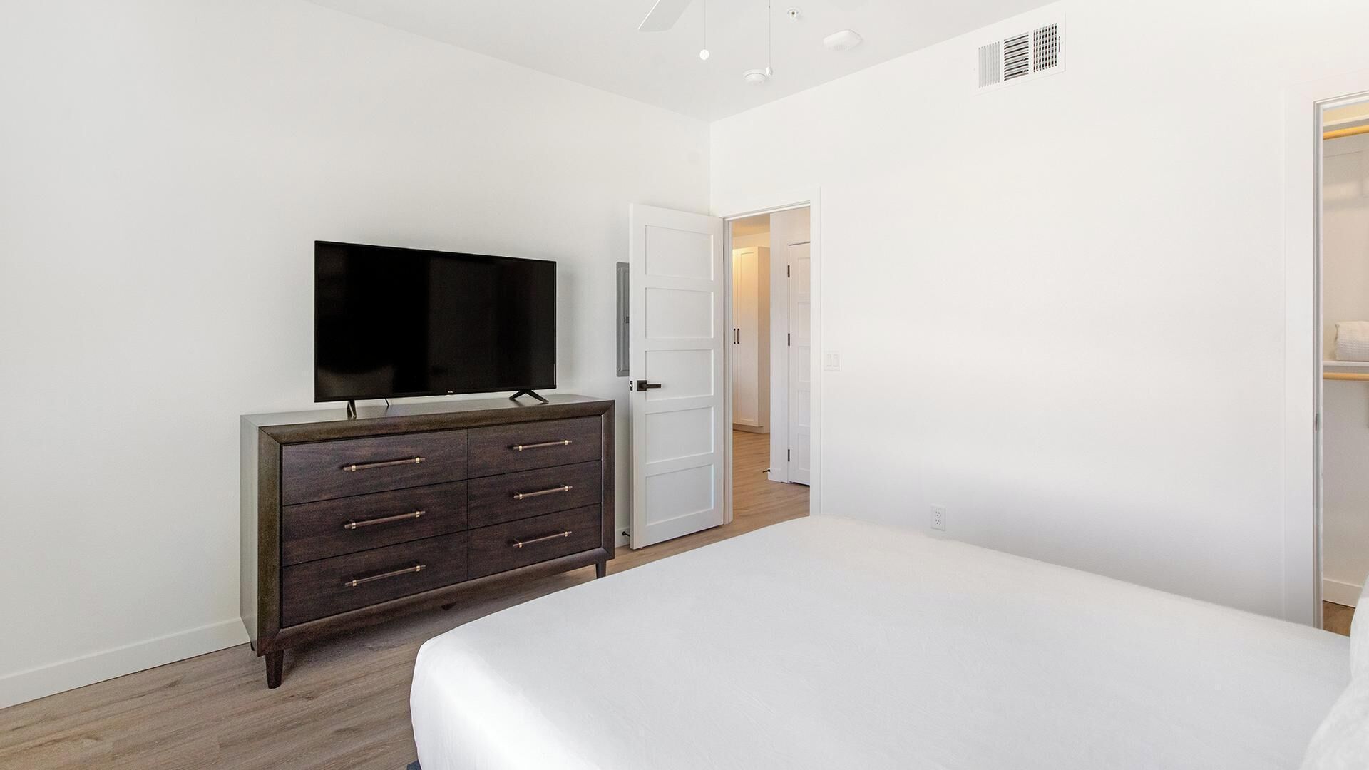 Quarto com cama, cômoda, televisão e porta que dá para outro espaço.