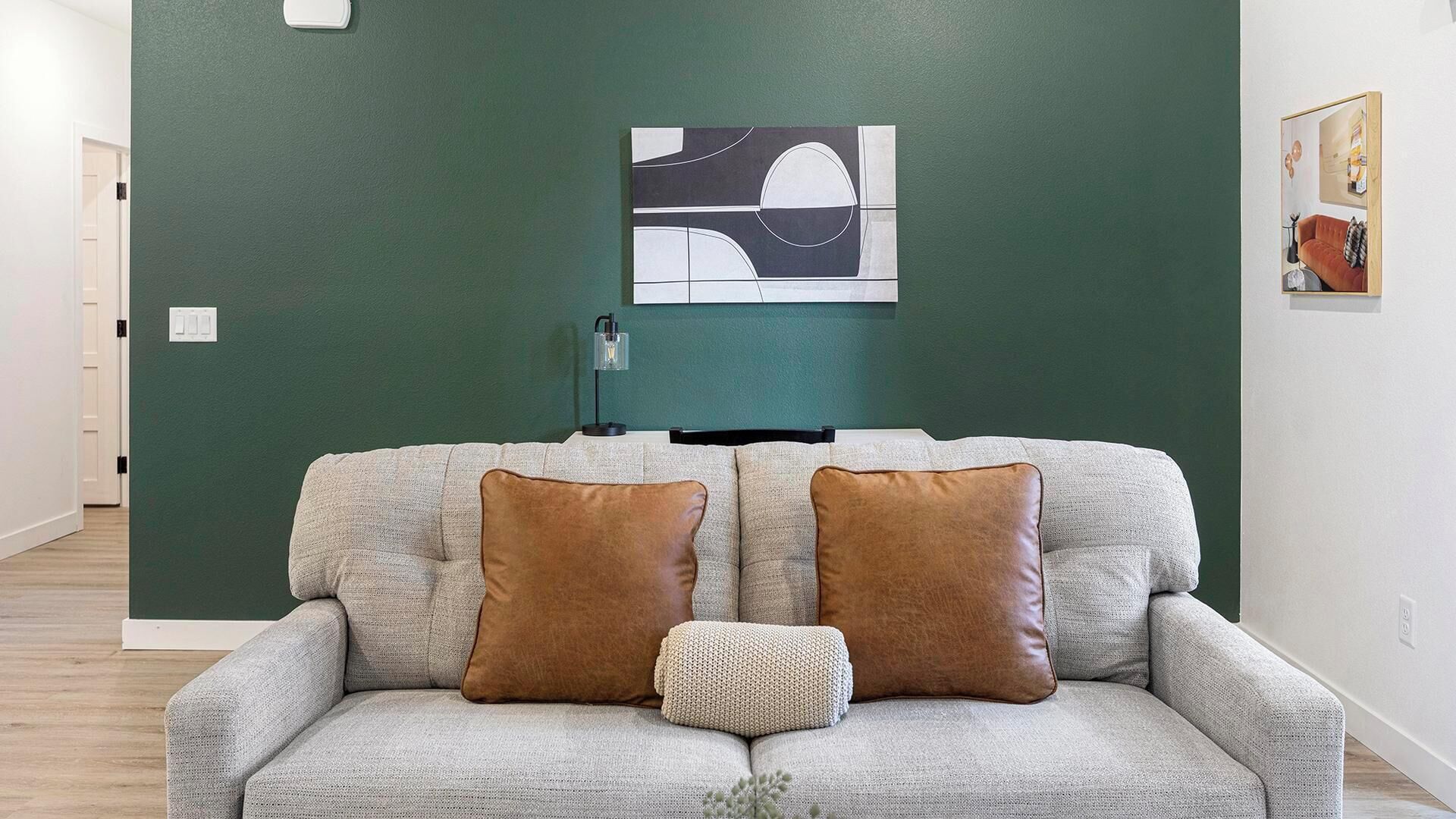 Una sala de estar con un sofá gris, dos cojines marrones y un cojín blanco pequeño, además de una obra de arte abstracta colgada en la pared.